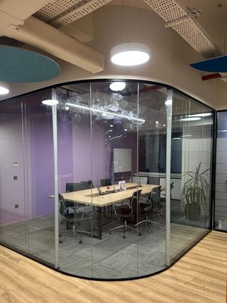 Masa ve sandalyelerin görüldüğü kavisli cam ofis bölmesi